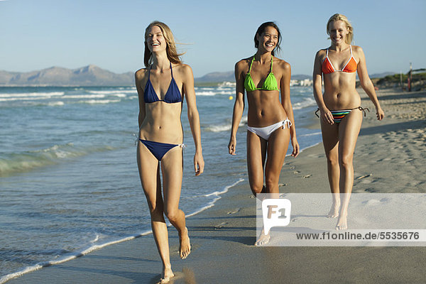 Frauen in Bikinis  die am Strand spazieren gehen.