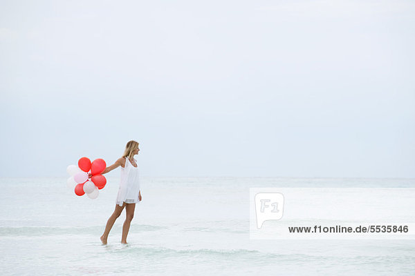 Eine Frau  die auf dem Wasser geht und einen Haufen Luftballons trägt.