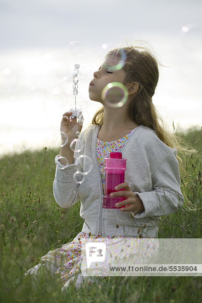Girl kneeling in field  blowing bubbles