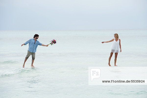 Couple walking on water towards each other  man holding out bouquet
