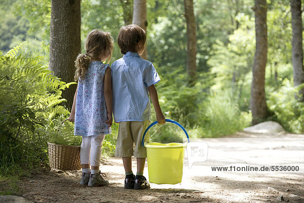 Kinder zusammen auf Waldweg  Mädchen tragen Korb und Junge tragen Eimer