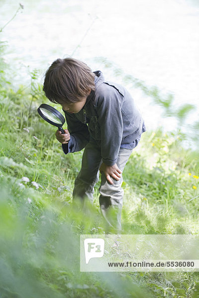 Boy looking at vegetation through magnifying glass