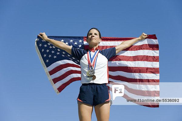 Athletin  die auf dem Podium geehrt wird und die amerikanische Flagge hochhält.
