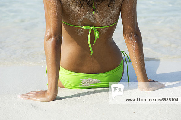 Frau im Bikini am Strand sitzend  Rückansicht  Mittelteil
