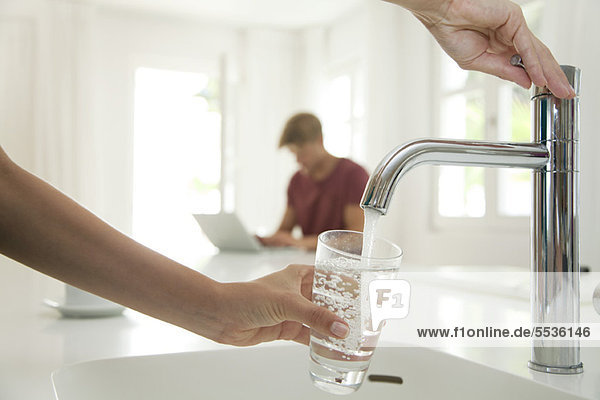 Woman filling glass of water at kitchen sink  cropped