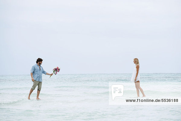 Couple walking on water towards each other  man holding out bouquet