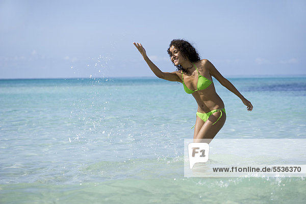 Junge Frau im Bikini spritzt Wasser im Ozean