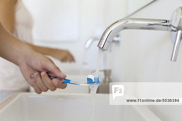 Man holding toothbrush under faucet  cropped