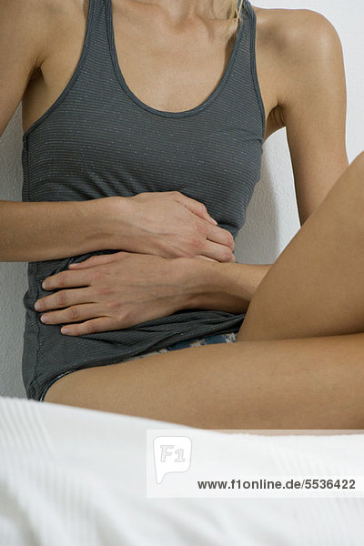 Woman sitting on bed  hands on stomach  mid section