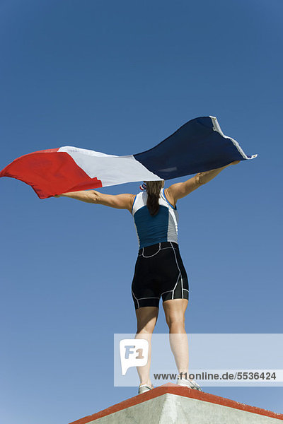 Eine Athletin auf dem Siegerpodest  die die französische Flagge hochhält.