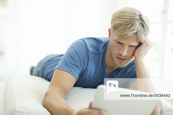 Auf dem Bauch liegender Mann beim Betrachten des digitalen Tabletts