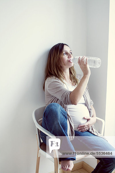 Schwangere Frau trinkt Wasser aus der Flasche