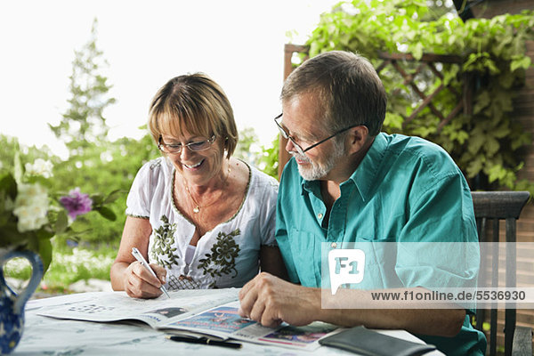 Glückliches Seniorenpaar löst gemeinsam Kreuzworträtsel in der Zeitung