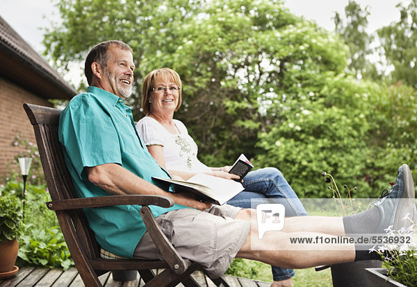 Glückliches Senior-Paar schaut weg  während es auf einem Stuhl im Garten sitzt.