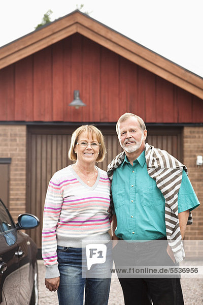 Älterer Mann mit Frau steht neben dem Auto vor der Garage