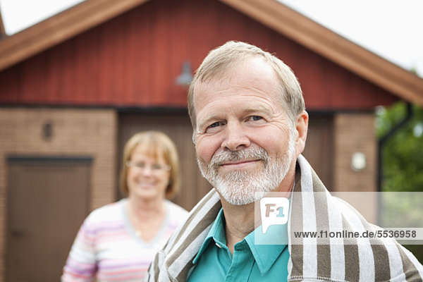 Nahaufnahme eines lächelnden älteren Mannes mit Frau im Hintergrund
