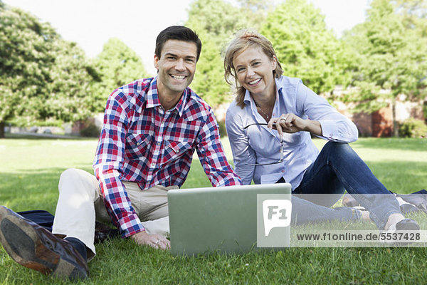 Porträt von fröhlichen Geschäftsleuten auf Rasen mit Laptop im Park