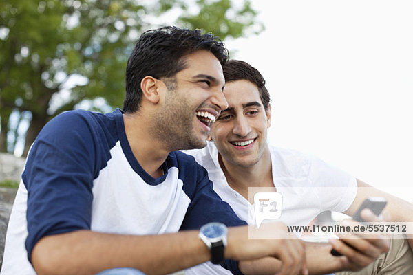 Fröhliche junge männliche Freunde  die etwas im Handy teilen