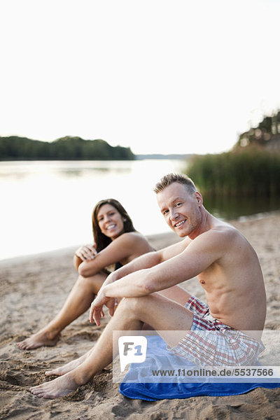 Porträt eines lächelnden heterosexuellen Paares auf Strandmatte sitzend