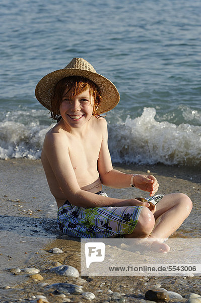 Junge sitzt am Strand im Wasser und freut sich