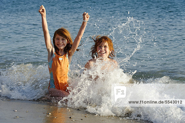 Kinder geschwister sitzen am Strand im Wasser und freuen sich in den Wellen