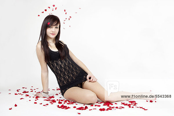 Young woman wearing black lingerie sitting amidst rose petals