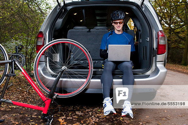 Radfahrer mit Laptop aus dem Kofferraum des Autos