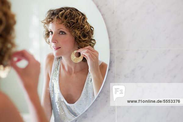 Mid adult woman putting on earrings in mirror