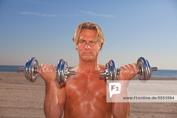 Bare-chested man on beach with weights