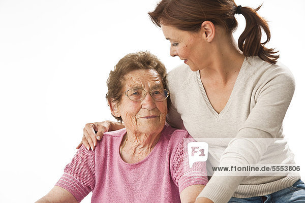 Lächelnde reife Frau umarmt sitzende alte Frau