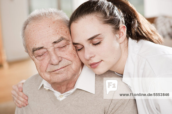 Junge Frau im Arztkittel umarmt Senior