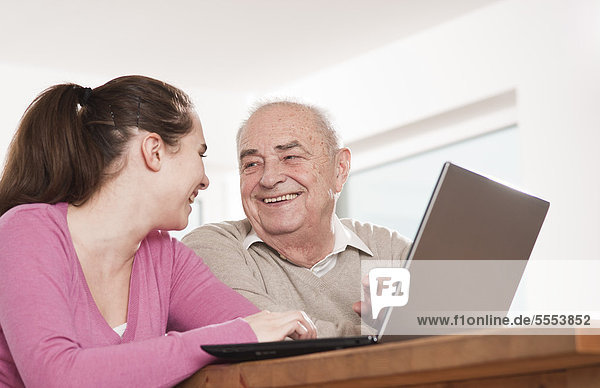 Fröhliche junge Frau und Senior am Laptop