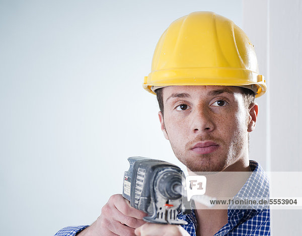 Young man wearing hard hat using drilling machine  portrait