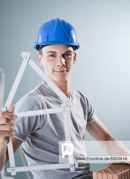 Young man wearing hard hat holding brick and folding rule in shape of a model house