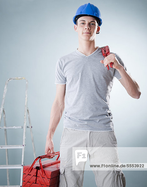 Junger Mann mit Bauhelm hält Werkzeug