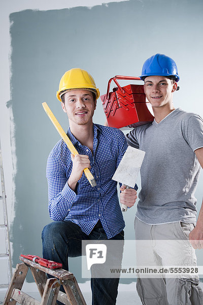 Two young men wearing hard hats holding tools