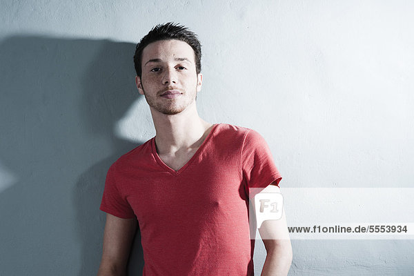 Young man wearing red T-shirt leaning against wall