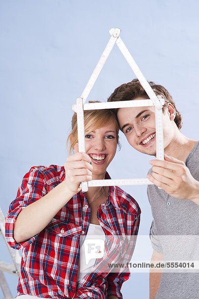 Smiling young couple holding folding rule in shape of a house