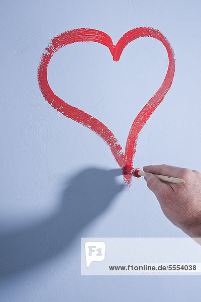 Hand malt ein rotes Herz an die Wand