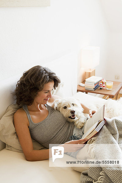 Woman reading with dog in bed