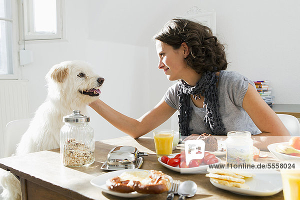 Frau streichelt Hund bei Tisch