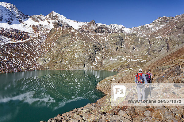 Hikers at Gruensee Lake while ascending Hintere Eggenspitze Mountain in the Ulten Valley above Lake Weissbrunn  looking towards Weissbrunnspitze Mountain with the summit of Hintere Eggenspitze Mountain on the left  Alto Adige  Italy  Europe