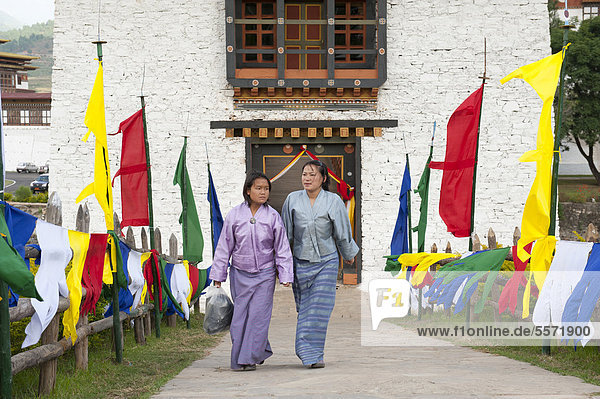 Two women dressed in traditional costume  coloured flags lining a path  fortress-monastery  Dzong  Punakha  the Himalayas  Kingdom of Bhutan  South Asia  Asia