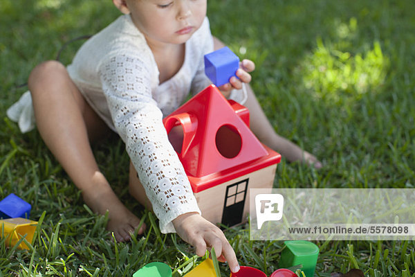 Kleines Mädchen auf Rasen sitzend  mit Spielzeug spielend