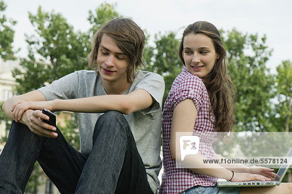 Young couple relaxing together outdoors with cell phone and laptop computer