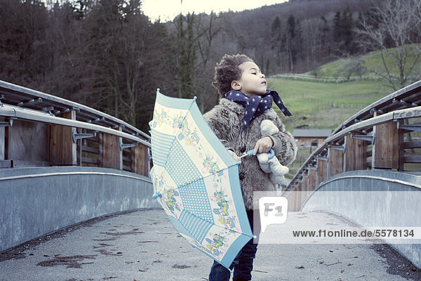 Kleines Mädchen auf der Brücke mit Regenschirm  schaut weg