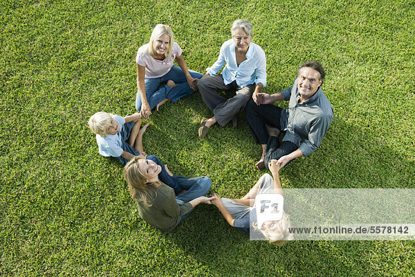 People sitting in circle on grass holding hands looking up at camera