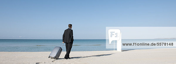 Geschäftsmann zieht Koffer am Strand  geht auf halboffene Tür zu
