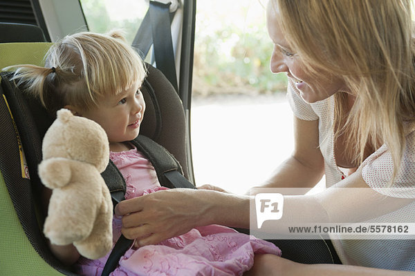 Mutter befestigt kleines Mädchen im Autositz