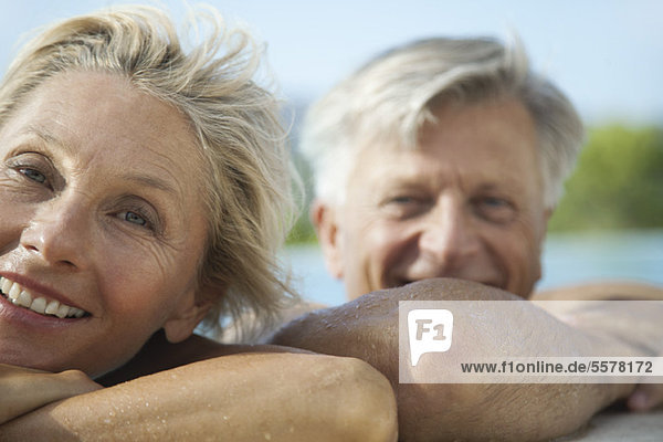 Mature couple resting their heads on side of pool  portrait
